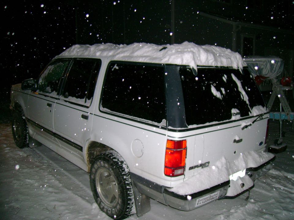 White 1995 Ford Explorer SUV in snow, rear view. Snow covers the roof and rear bumper