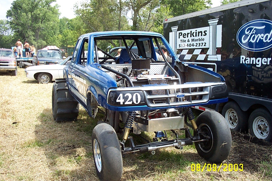 Blue modified Ford Ranger pickup truck with large rear tires and number 420 on the grille. Ford Ranger trailer is behind it