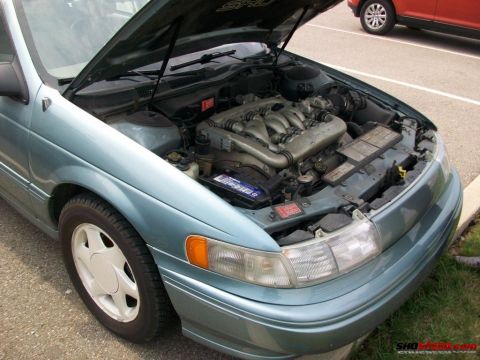 1993 Ford Taurus - The engine bay of a teal 1993 Ford Taurus sedan is open for viewing, with another vehicle visible in the background.