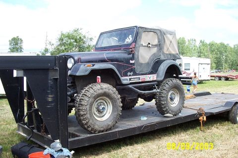 1996 Ford Bronco - A lifted Jeep CJ-7 is loaded onto a trailer, ready for transport.