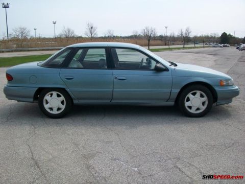 1993 Ford Taurus - This light blue sedan is parked on a cracked asphalt lot with trees and utility poles in the background.