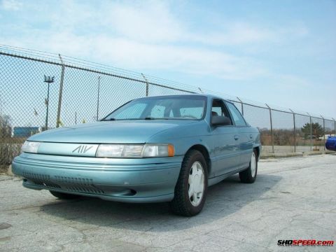 1993 Ford Taurus - This teal sedan has a distinctive grille emblem and appears to be from the early 1990s.