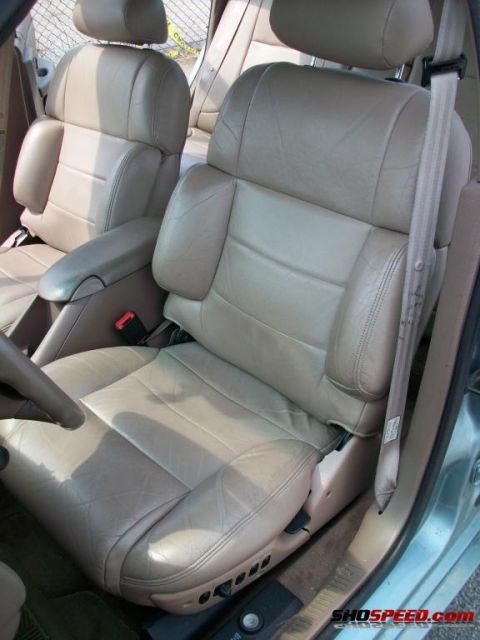 1993 Ford Taurus - Interior view of tan leather bucket seats and armrest with a seatbelt.