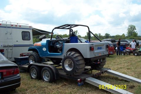 1996 Ford Bronco - A modified Jeep CJ-7 with oversized tires is loaded onto a trailer, with a camper and other vehicles in the background.