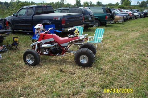 1996 Ford Bronco - Three-wheeled ATV with large rear tires parked in a grassy field with other vehicles behind it.