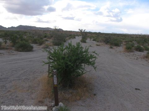 1996 Ford C-350 (Centurion Conversions) - A trail marker stands in a dusty, arid landscape with sparse vegetation and distant mountains.