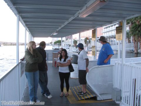1996 Ford C-350 (Centurion Conversions) - Several people stand on a wooden pier under a metal roof, with buildings and palm trees visible in the background.