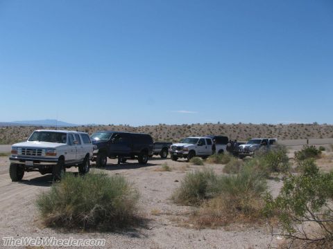 1996 Ford C-350 (Centurion Conversions) - A convoy of SUVs and trucks are parked on a dirt road in a dry, arid landscape under a clear blue sky.