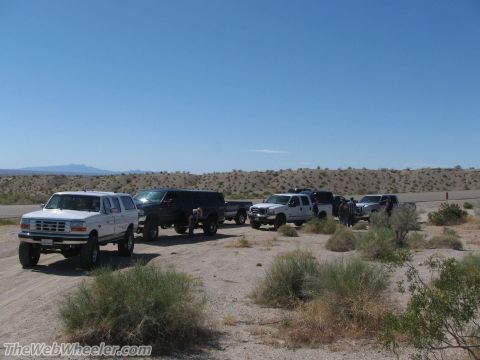 1996 Ford C-350 (Centurion Conversions) - A convoy of trucks and SUVs, including a white Ford Bronco, are parked in a desert landscape under a clear blue sky.