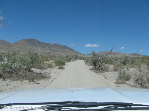 1996 Ford C-350 (Centurion Conversions) - View from inside a vehicle driving on a dusty desert road with scrub brush and mountains ahead.