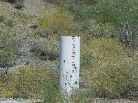 1996 Ford C-350 (Centurion Conversions) - A weathered marker indicates the state line in a dry, brushy landscape.