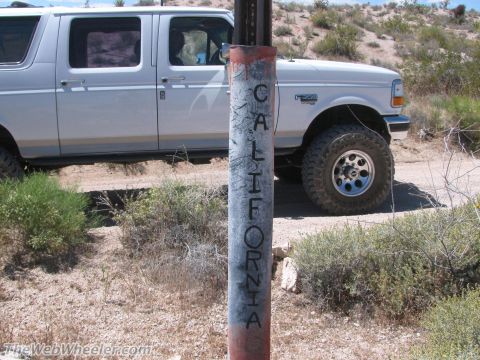 1996 Ford C-350 (Centurion Conversions) - A lifted white Ford F-Series SUV is parked off-road next to a weathered post marking a state border.