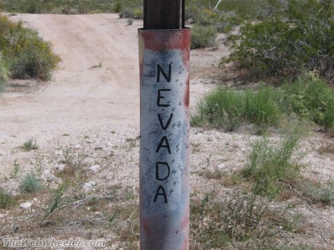 1996 Ford C-350 (Centurion Conversions) - A weathered post marks the Nevada state line on a dusty desert road.