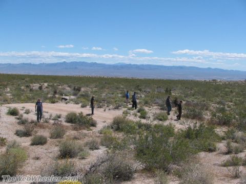 1996 Ford C-350 (Centurion Conversions) - Several people walk across a dry, brush-covered landscape under a bright blue sky with distant mountains.