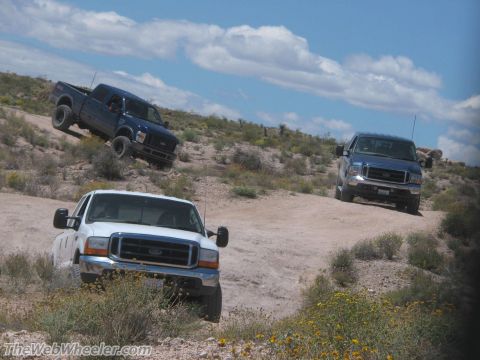 1996 Ford C-350 (Centurion Conversions) - Multiple Ford trucks navigate a dusty desert trail under a partly cloudy sky.