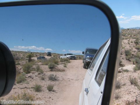 1996 Ford C-350 (Centurion Conversions) - Several trucks drive on a dirt road through a desert landscape.