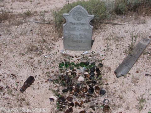 1996 Ford C-350 (Centurion Conversions) - A tombstone marks a grave in a desert setting, surrounded by broken glass bottles and a piece of wood.