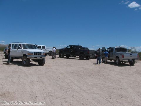 1996 Ford C-350 (Centurion Conversions) - Several pickup trucks are parked in a dirt lot under a clear blue sky.