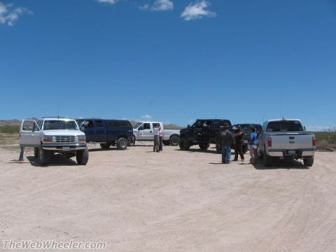 1996 Ford C-350 (Centurion Conversions) - Several lifted trucks and SUVs are parked in a dusty, desert area under a bright blue sky.