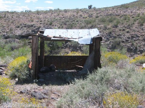 1996 Ford C-350 (Centurion Conversions) - An old, weathered wooden structure stands in a dry, hilly landscape under a bright blue sky.