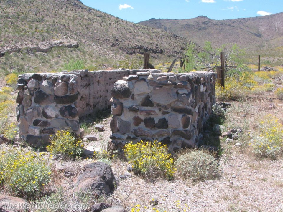 Old stone building ruins in a dry, hilly area with sparse vegetation and a bright blue sky