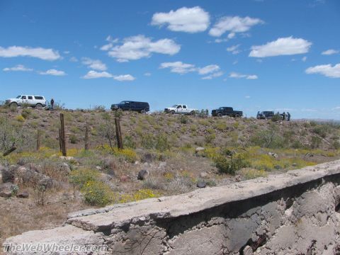 1996 Ford C-350 (Centurion Conversions) - A convoy of SUVs and trucks traverses a , arid landscape under a bright, cloud-dotted sky.