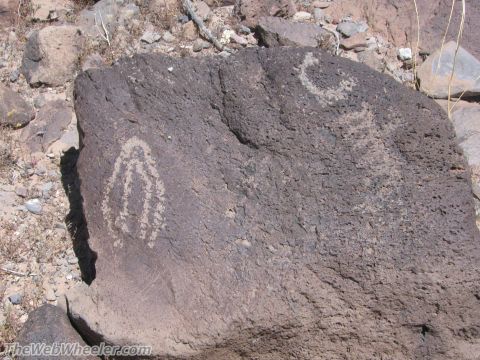 1996 Ford C-350 (Centurion Conversions) - Ancient petroglyphs are etched into a dark rock formation in a desert environment.
