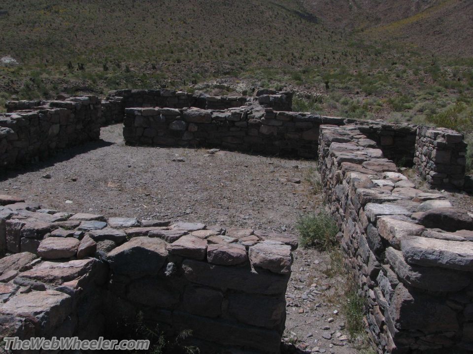 Stone ruins in a dry, hilly landscape. The walls are made of rough, stacked stones