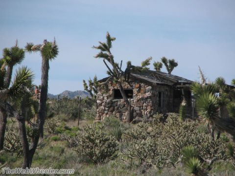 1996 Ford C-350 (Centurion Conversions) - An old stone structure sits abandoned in a desert landscape, overgrown with vegetation.