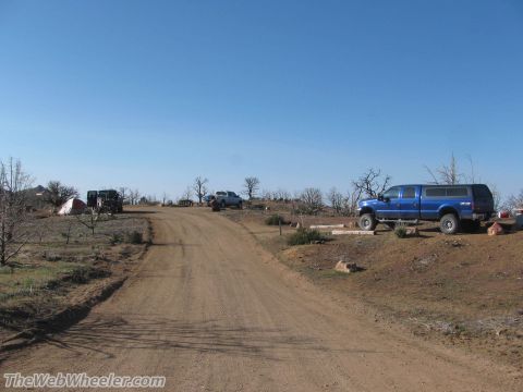 1996 Ford C-350 (Centurion Conversions) - A campsite scene with two pickup trucks and a tent set up on a dirt road.