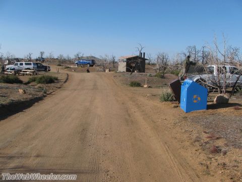 1996 Ford C-350 (Centurion Conversions) - A view of a campsite with several trucks parked around a dirt road and a small building.