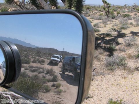 1996 Ford C-350 (Centurion Conversions) - Two SUVs travel off-road through a desert landscape, seen from the side mirror.