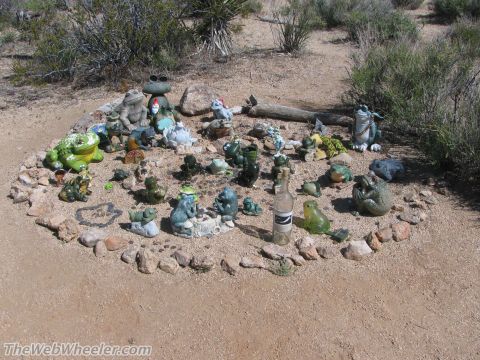 1996 Ford C-350 (Centurion Conversions) - A collection of frog statues and a bottle are arranged in a circle on the sandy ground.