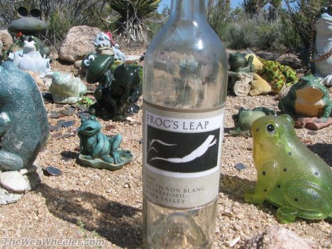 1996 Ford C-350 (Centurion Conversions) - A collection of frog statues surrounds a wine bottle in a dry, outdoor setting.