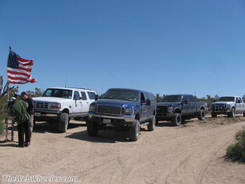 1996 Ford C-350 (Centurion Conversions) - Several trucks and an SUV are parked in a desert landscape under a clear blue sky.