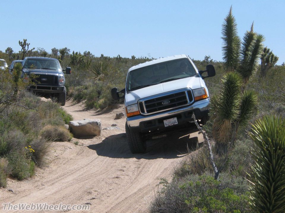 White Ford F-Series truck driving on a dirt trail, front 3/4 view. License plate reads 6371464