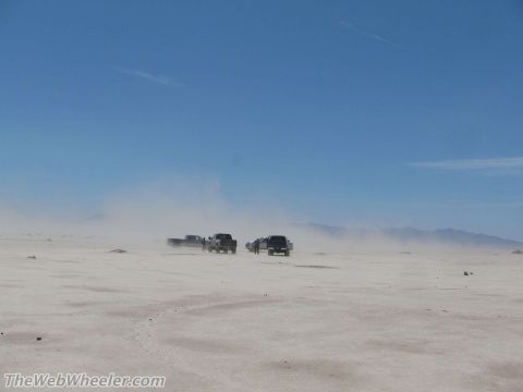 1996 Ford C-350 (Centurion Conversions) - Multiple trucks traverse a dry, dusty plain with mountains in the distance.