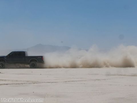 1996 Ford C-350 (Centurion Conversions) - A pickup truck drifts across a dry lake bed, creating a massive plume of dust against a clear blue sky.