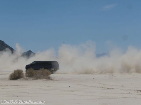 1996 Ford C-350 (Centurion Conversions) - SUV driving through dust on a dry, open plain with mountains in the distance.