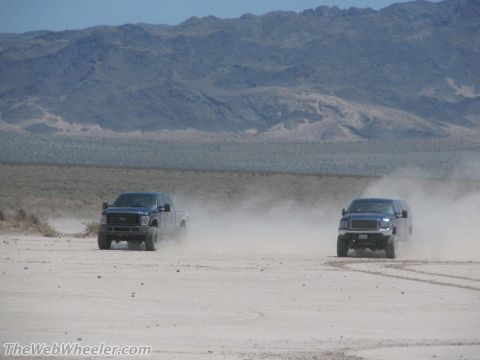 1996 Ford C-350 (Centurion Conversions) - Two SUVs kick up dust as they drive across a dry, barren landscape under a clear sky.