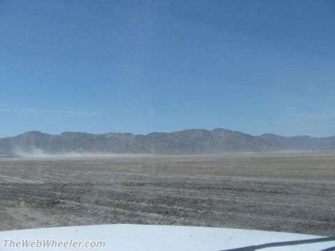 1996 Ford C-350 (Centurion Conversions) - A wide, arid landscape stretches out towards distant mountains, with dust kicked up in the air.