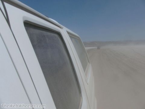 1996 Ford C-350 (Centurion Conversions) - Two vehicles travel on a dirt road, kicking up dust under a clear blue sky.