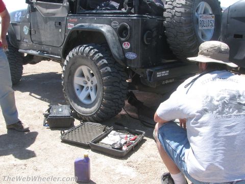 1996 Ford C-350 (Centurion Conversions) - A person works on a Jeep Wrangler, with tools laid out on the ground.