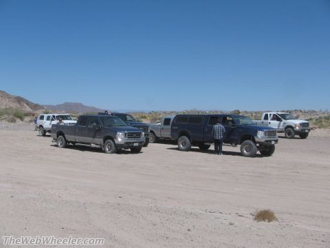 1996 Ford C-350 (Centurion Conversions) - Multiple pickup trucks are parked in a desert area under a clear blue sky.