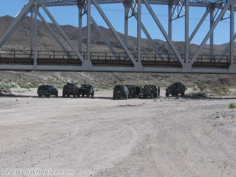 1996 Ford C-350 (Centurion Conversions) - A group of off-road vehicles are gathered under a large bridge in a dry, mountainous area.