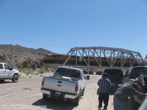1996 Ford C-350 (Centurion Conversions) - A silver pickup truck is parked on a dirt road with a train crossing a bridge in the background.