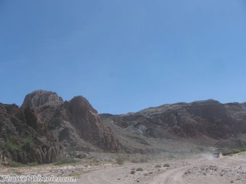 1996 Ford C-350 (Centurion Conversions) - A vehicle travels on a dusty dirt road through a desert landscape with mountains under a clear blue sky.
