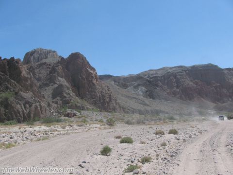 1996 Ford C-350 (Centurion Conversions) - A vehicle kicks up dust on a remote desert road, with mountains under a clear blue sky.