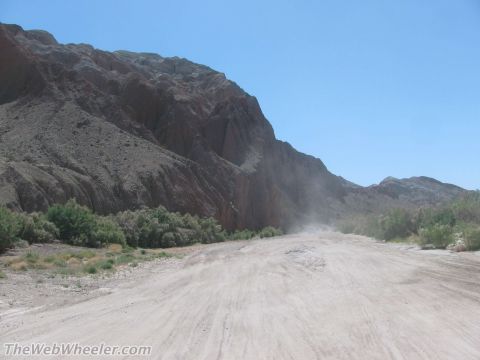 1996 Ford C-350 (Centurion Conversions) - A dust cloud billows up from a dirt road winding through a desert landscape with rocky mountains in the background.