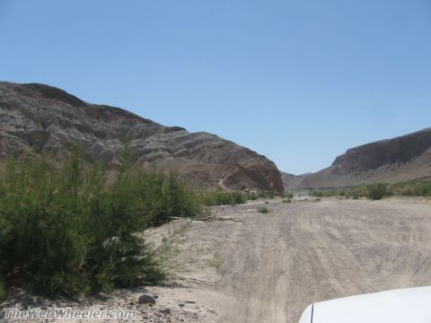 1996 Ford C-350 (Centurion Conversions) - A white vehicle travels down a dusty road through a desert canyon, with mountains on either side.
